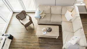Ett vardagsrum med en beige soffa, en fåtölj i rotting, ett soffbord i trä och ett litet sidobord.