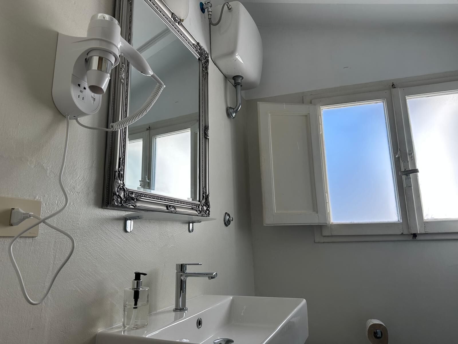 A bathroom with a large mirror, a sink, a faucet, and a window.