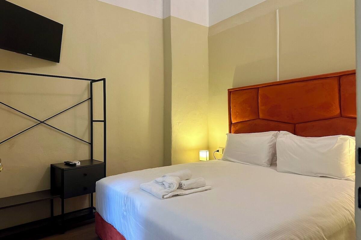 Ein Hotelzimmer mit einem Bett, einem an der Wand montierten Fernseher, einem Nachttisch und einem Beistelltisch.