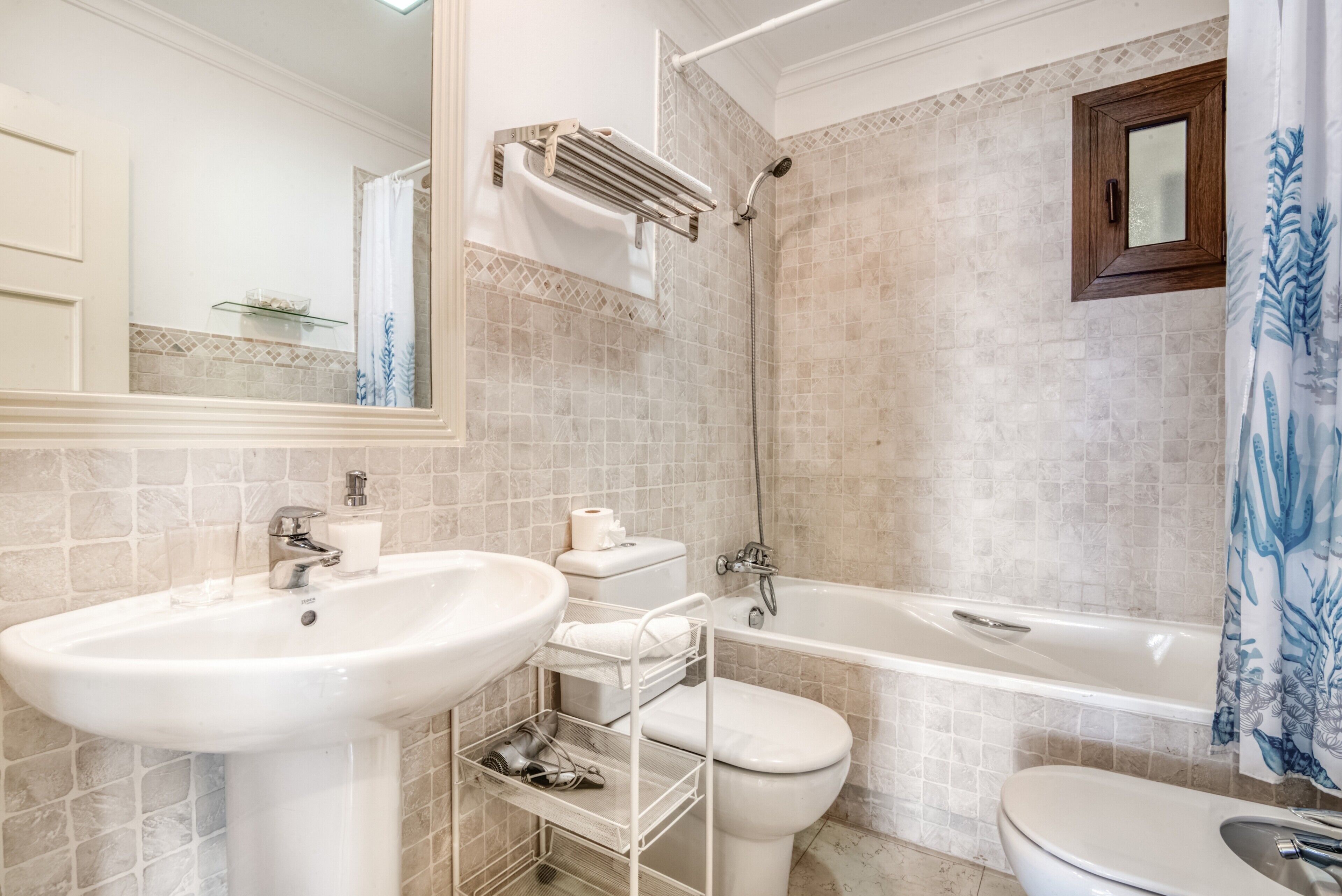 Une salle de bain avec un lavabo, des toilettes et une baignoire, des murs carrelés et un miroir.