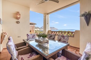 Un balcone con mobili in vimini, un tavolo con piano in vetro e una pianta in vaso.