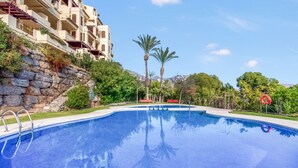 Une piscine bordée d’un mur en pierre et entourée de palmiers, le tout adossé à un immeuble doté de balcons.