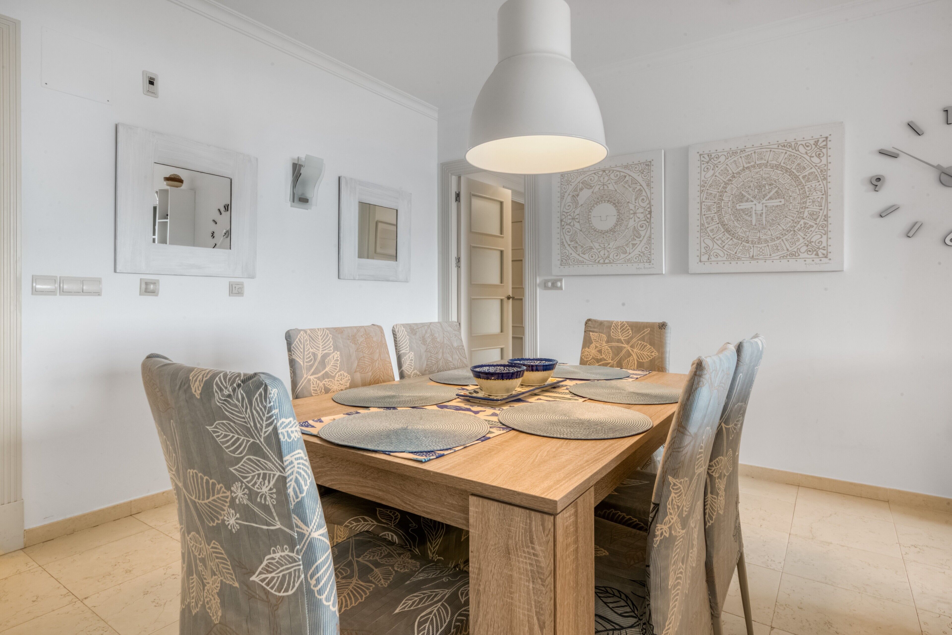 A dining area with a wooden table, chairs, a hanging light fixture, and decorative wall art.