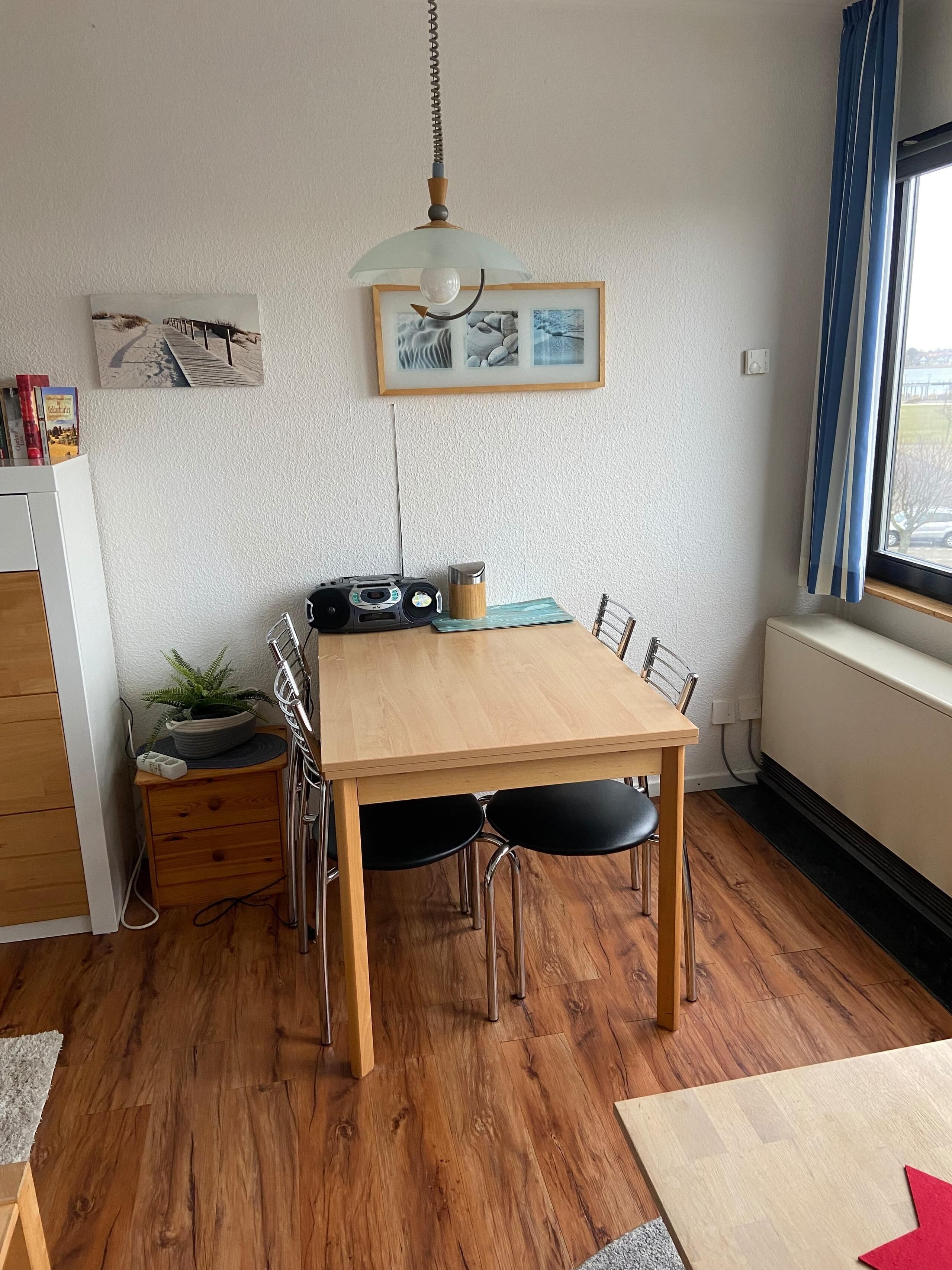 Een eetruimte met een houten tafel, stoelen, een hanglamp en een raam met gordijnen.