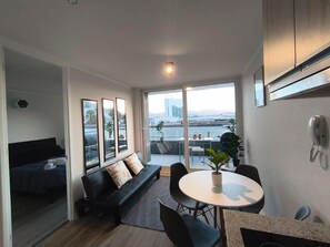 A modern living room with a sofa, a dining table, and a view of a cityscape through large windows.