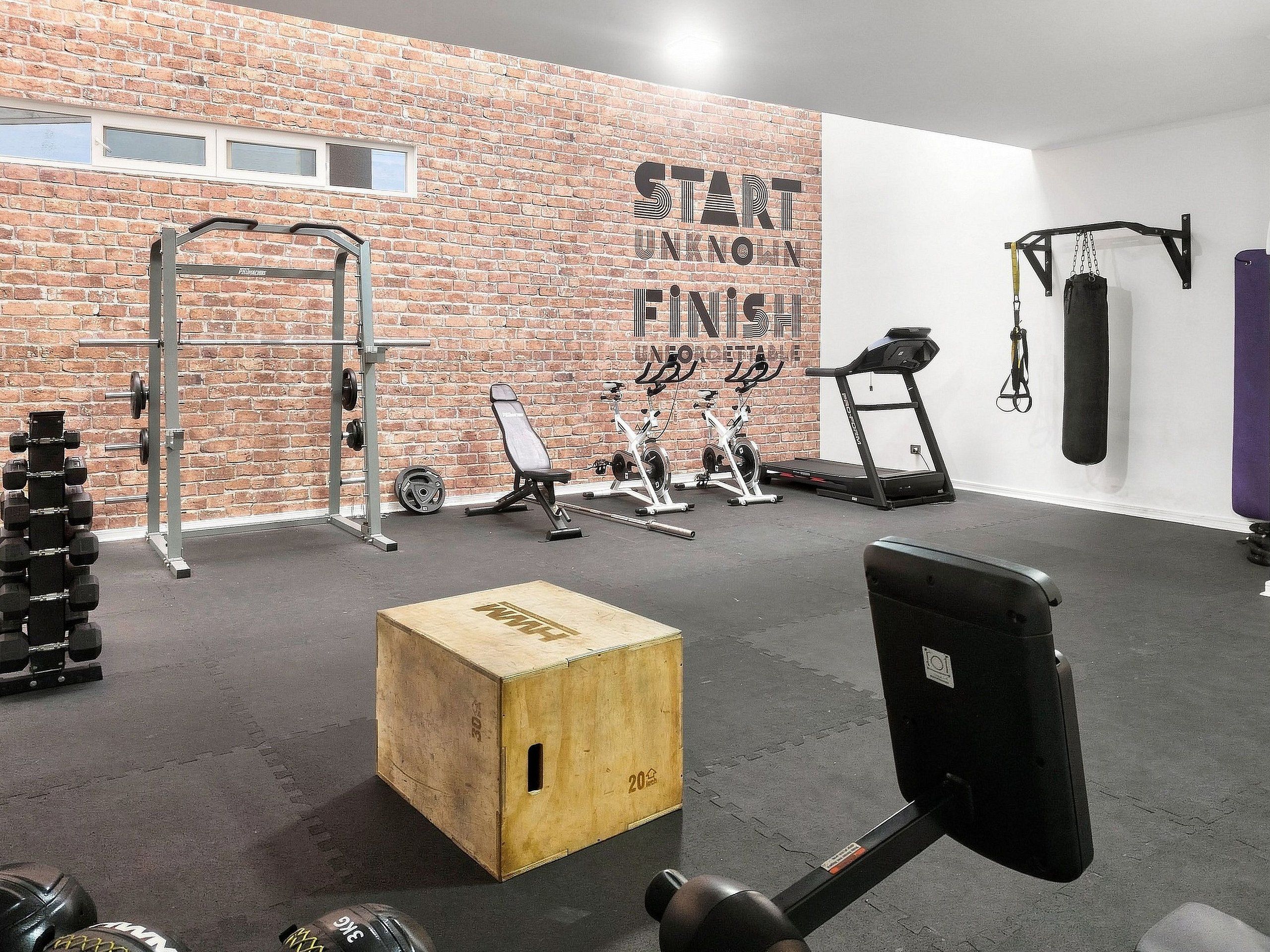 A gym with a brick wall, weightlifting equipment, cardio machines, and a motivational quote.