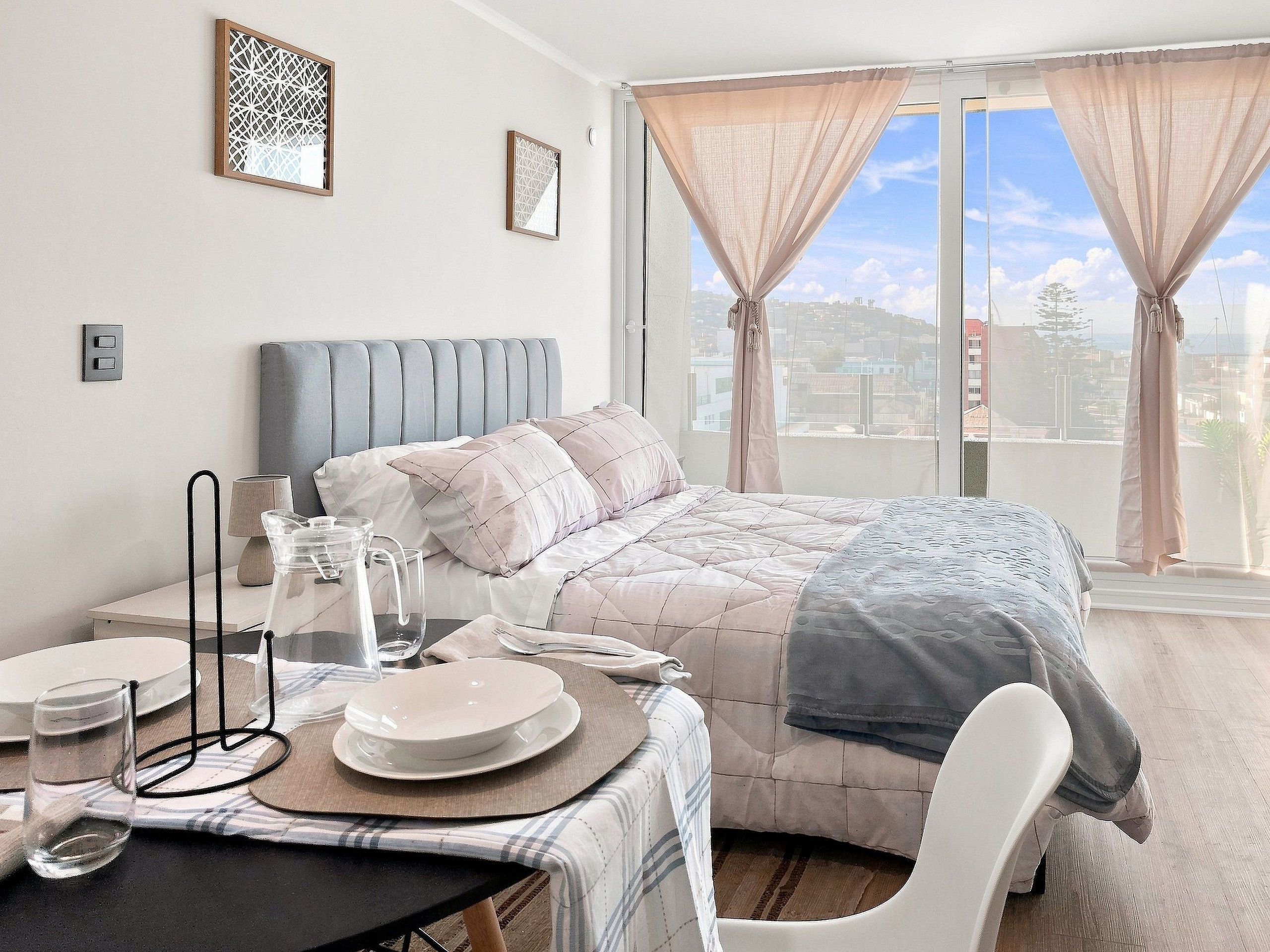 A bedroom with a bed, bedside table, and a view of the city through large windows.