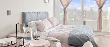 A bedroom with a bed, bedside table, and a view of the city through large windows.