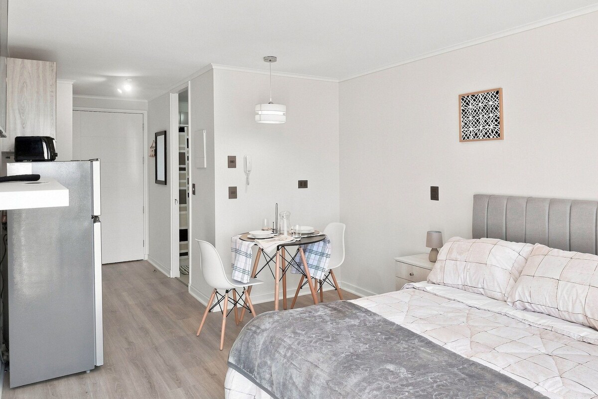 A modern bedroom with a bed, bedside table, and a small desk area with chairs.