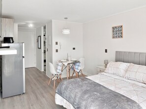 A modern bedroom with a bed, bedside table, and a small desk area with chairs. - Oceana Suites Edificio HA (Coquimbo)