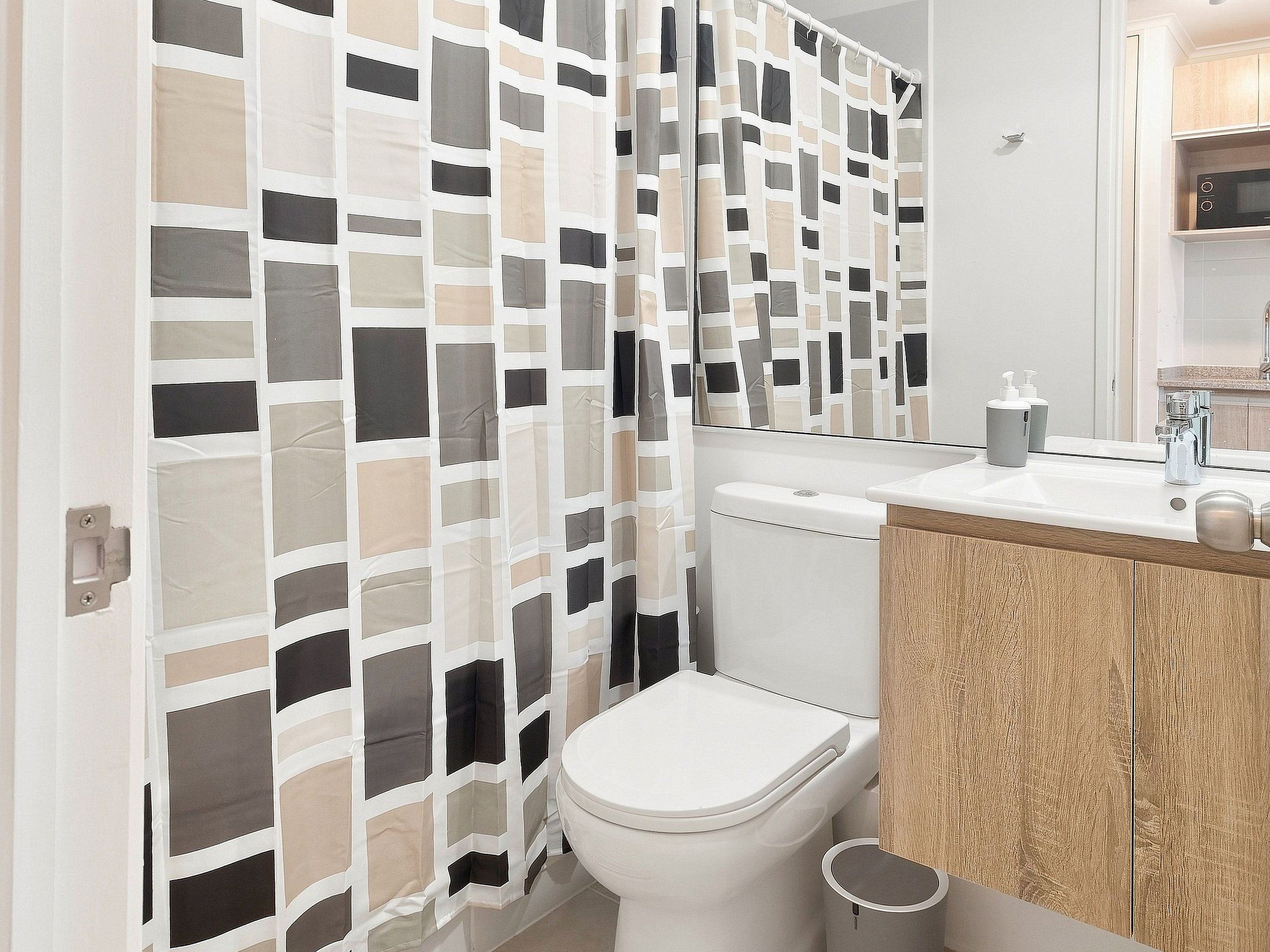 Une salle de bain au design moderne, comprenant des toilettes, un lavabo avec un miroir et un rideau de douche à motifs géométriques.