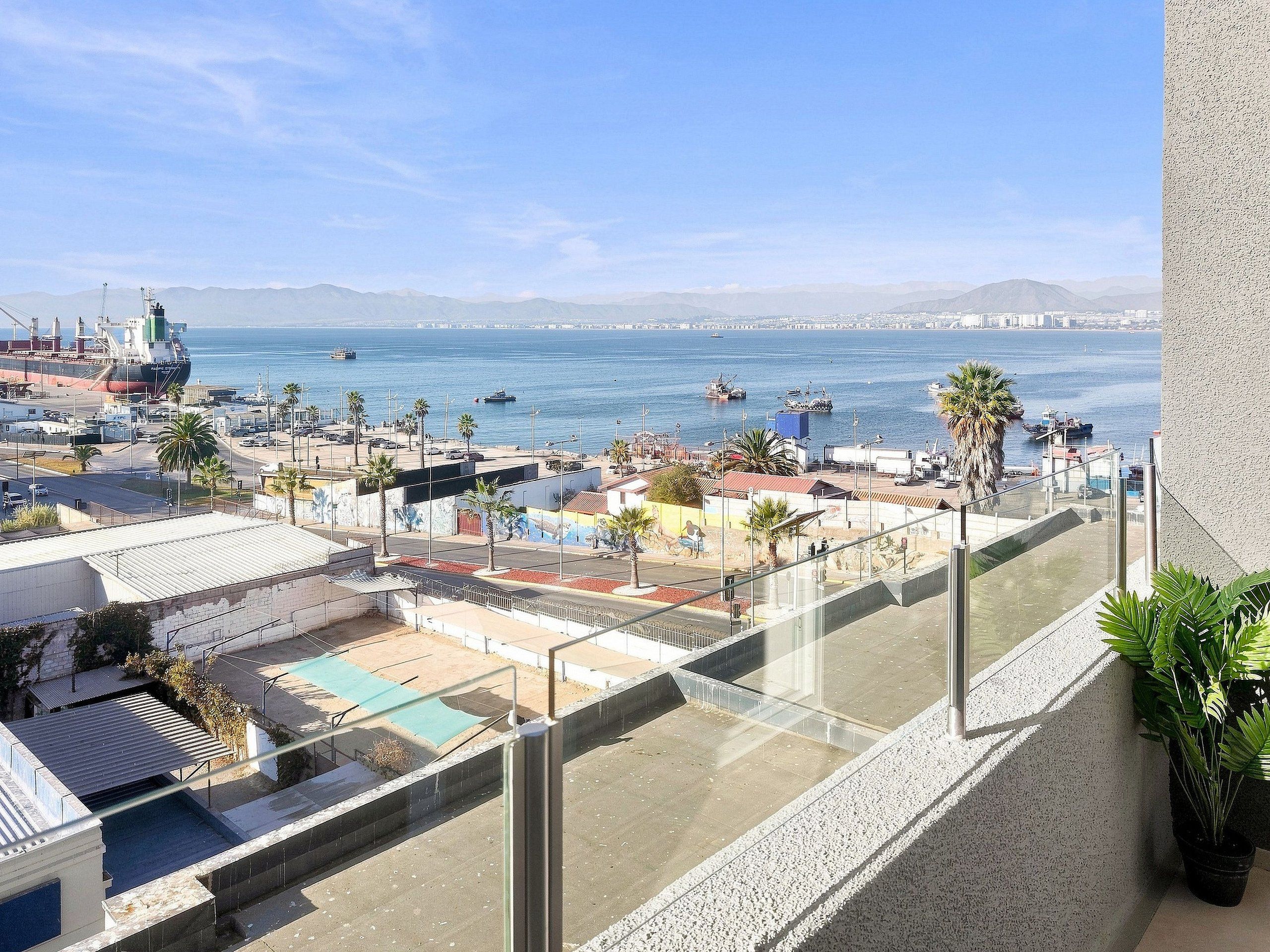 Un balcon offrant une vue sur un port, des navires et des montagnes lointaines.