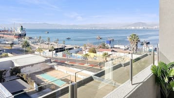 Un balcón con vista a un puerto, barcos y montañas lejanas.
