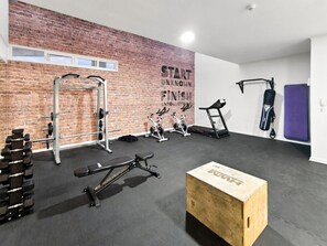 A gym with a brick wall, weightlifting equipment, a treadmill, and a punching bag.