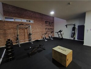A gym with a brick wall, weightlifting equipment, cardio machines, and a wooden box.