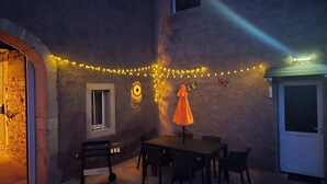 A patio area with a table and chairs, a small grill, decorative lights, and a butterfly wall decoration.
