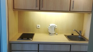 A small kitchen with wooden cabinets, a kettle, a sink, and a stove. - Pure relaxation on the Baltic Sea: vacation apartment with sandy beach right on the doorstep! (Fehmarn)