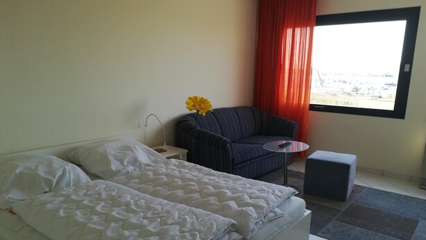 A hotel room with a bed, a small table, a chair, and a window with curtains. - Pure relaxation on the Baltic Sea: vacation apartment with sandy beach right on the doorstep! (Fehmarn)