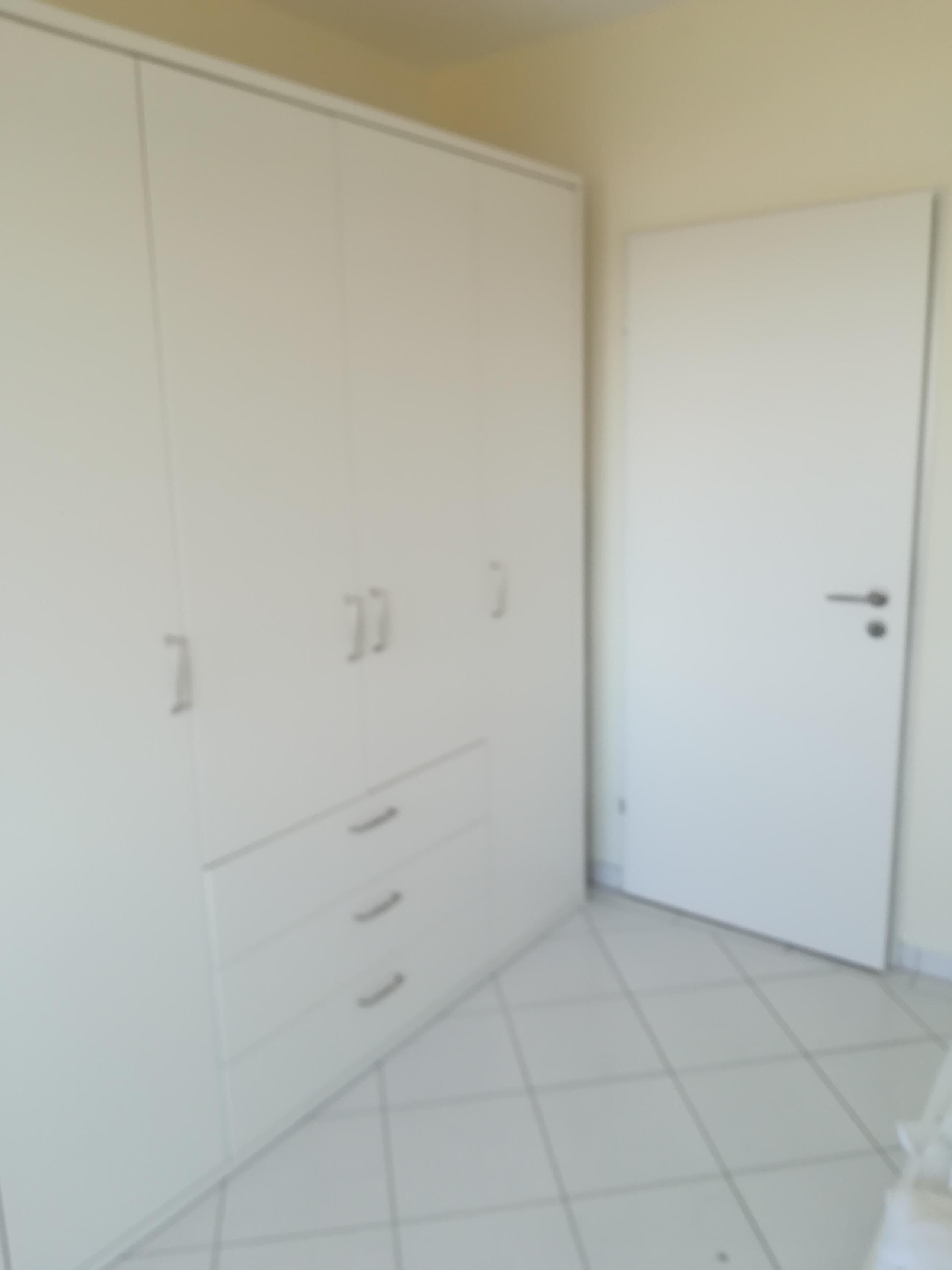 A room with a large wardrobe, a door, and tiled flooring.