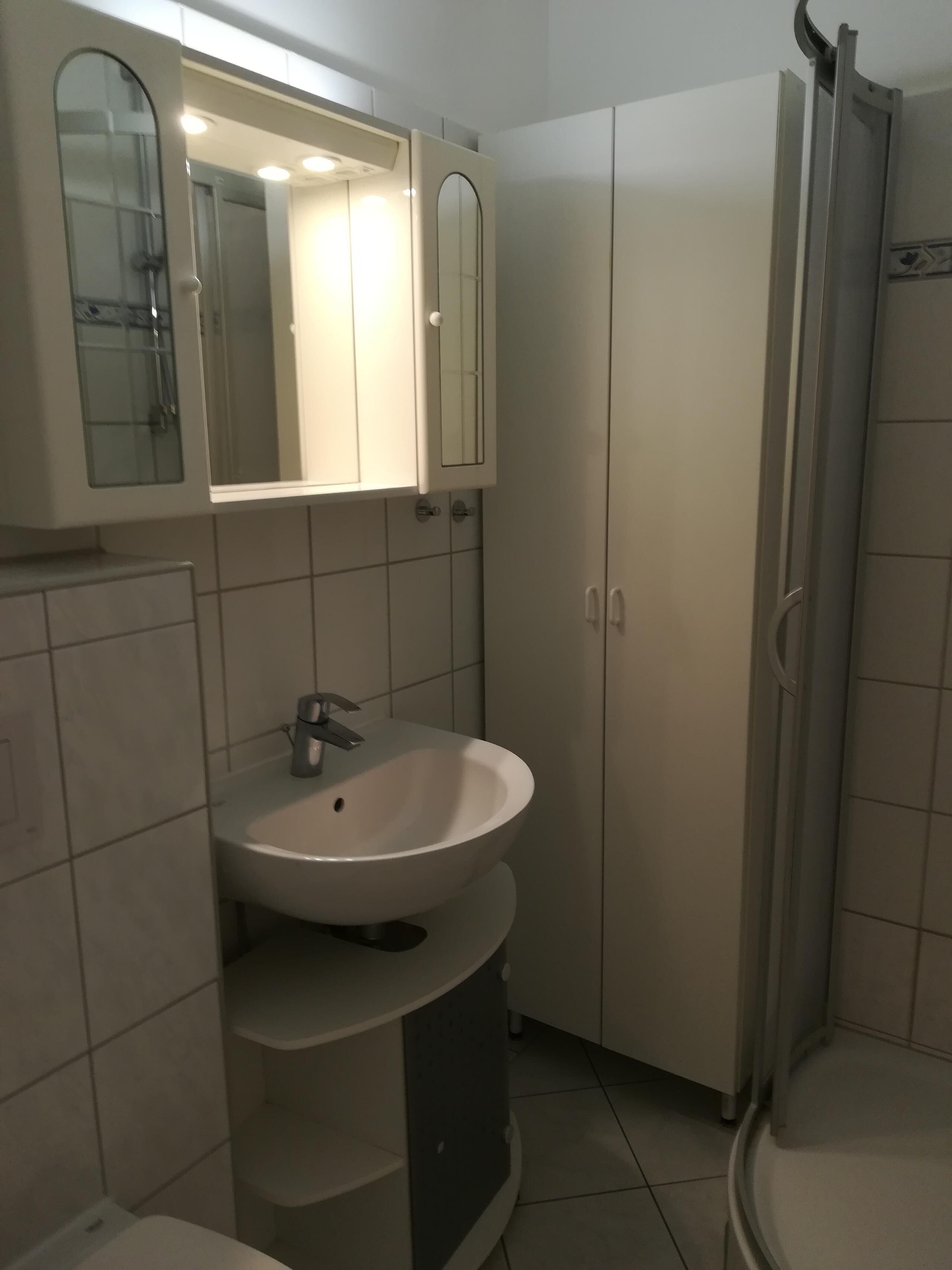 A bathroom with a white sink, mirror, and cabinet.