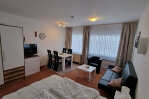 Et hotelværelse med seng, fjernsyn, spisebord med stole, sofa og et vindue med gardiner.