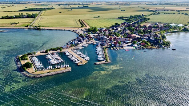 An aerial view of a coastal town with a marina, houses, and fields. - Relaxation and adventure at Deichhuus: your vacation paradise on the Baltic Sea! (Fehmarn)