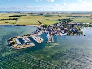 Luchtbeeld van een kustplaatsje met een jachthaven, huizen en velden.