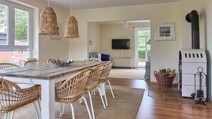 A spacious living area with a wooden dining table, wicker chairs, a fireplace, and a television. - Relaxation and adventure at Deichhuus: your vacation paradise on the Baltic Sea! (Fehmarn)