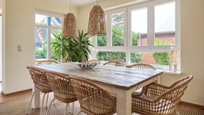 A dining area with a wooden table, wicker chairs, and hanging wicker lamps. - Relaxation and adventure at Deichhuus: your vacation paradise on the Baltic Sea! (Fehmarn)
