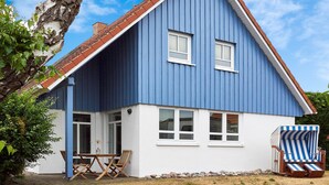 A two-story house with a blue exterior and a red roof. There are two windows on the upper floor and a door on the lower floor. - Relaxation and adventure at Deichhuus: your vacation paradise on the Baltic Sea! (Fehmarn)
