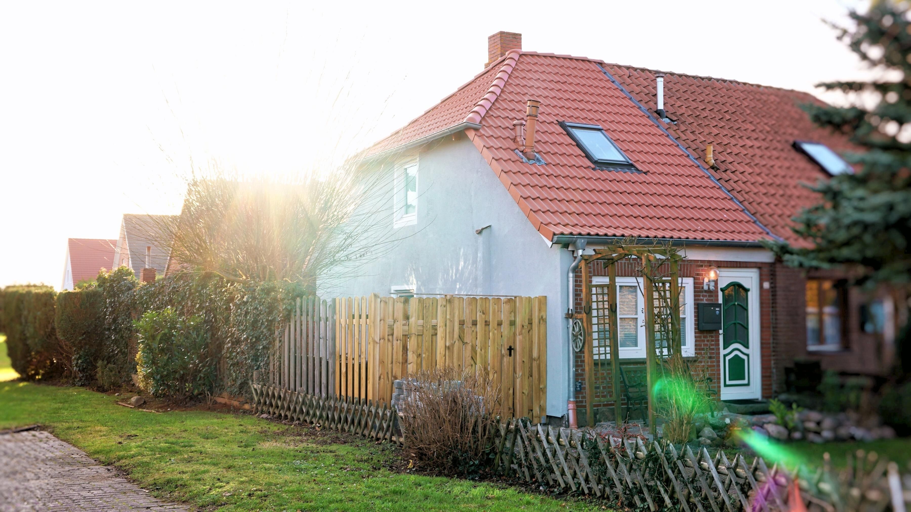 Een huis met een rode pannendak, een houten omheining en een tuin.