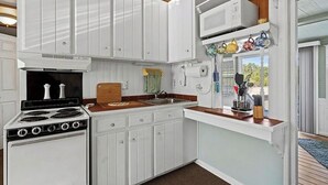 A compact kitchen with white cabinetry, a stove, a microwave, and a window with a view. - Wonderful 3-bedroom house with AC in welcoming Cross Hill (Cross Hill)