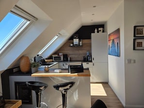 A modern kitchen with a skylight, a dining area with bar stools, and a kitchen island. - Toplicht Rental – Harbor View & Sauna in Orth (Schwanitz) with Balcony and Lake View   (Fehmarn OT Orth)