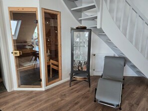 A room with a wooden floor, a glass door leading to another room, a black cabinet with glassware, and a grey chair. - Toplicht Vacation Rental – Harbor View & Sauna in Orth (Schwanitz) with a Balcony and Lake View (Fehmarn OT Orth)