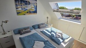Un dormitorio con una cama grande, un cuadro de veleros, un tragaluz y vistas al exterior.