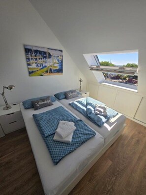 A bedroom with a large bed, a painting of sailboats, a skylight, and a view of the outside. - Toplicht Vacation Rental – Harbor View & Sauna in Orth (Schwanitz) with a Balcony and Lake View (Fehmarn OT Orth)