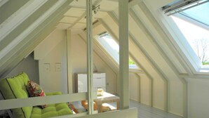 Ein Dachzimmer mit hohen Decken, einem Oberlicht, einer grünen gepolsterten Bank und einem kleinen Tisch mit einer Lampe.