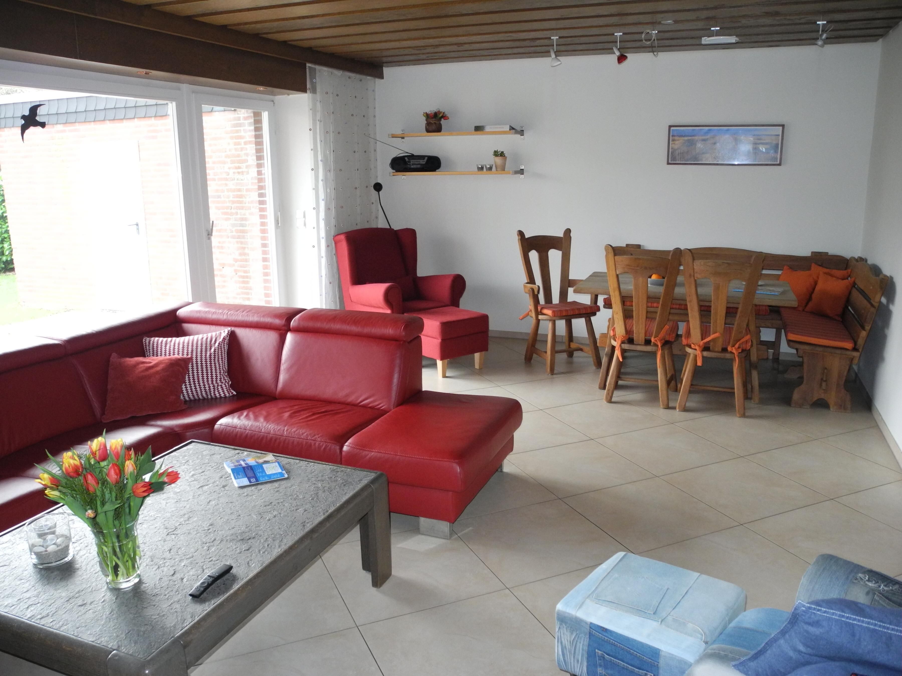 Un salon avec un canapé rouge, une table basse ornée d’un vase de fleurs, une table à manger avec des chaises et un téléviseur posé sur un meuble.