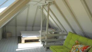 Ein Schlafzimmer im Dachgeschoss mit einem Etagenbett, einem grünen Sofa und einem farbenfrohen Kissen.