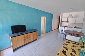 A room with a TV on a wooden cabinet, a bed with a patterned blanket, and a kitchenette with white cabinets and a hanging light. - Staying in the Marina di Bibbona Apartments combines the convenience of feeling at home with the comfort of a holiday in a green setting, just steps from the sea and all the main amenities. With its pleasant atmosphere, <b>Marina di Bibbona</b> combines  (Marina di Bibbona)