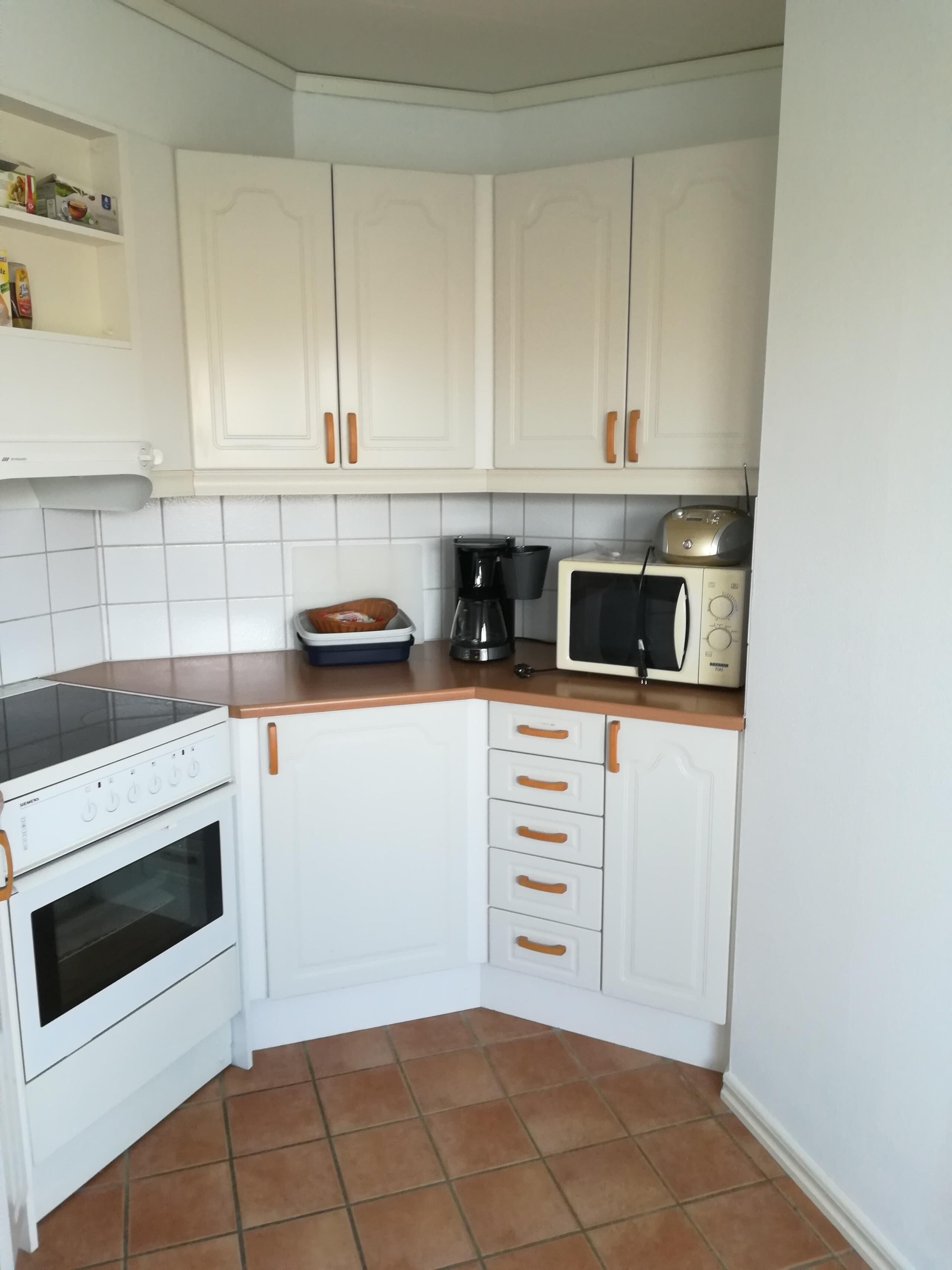 A compact kitchen with white cabinets, a built-in oven, a microwave, and a coffee maker.