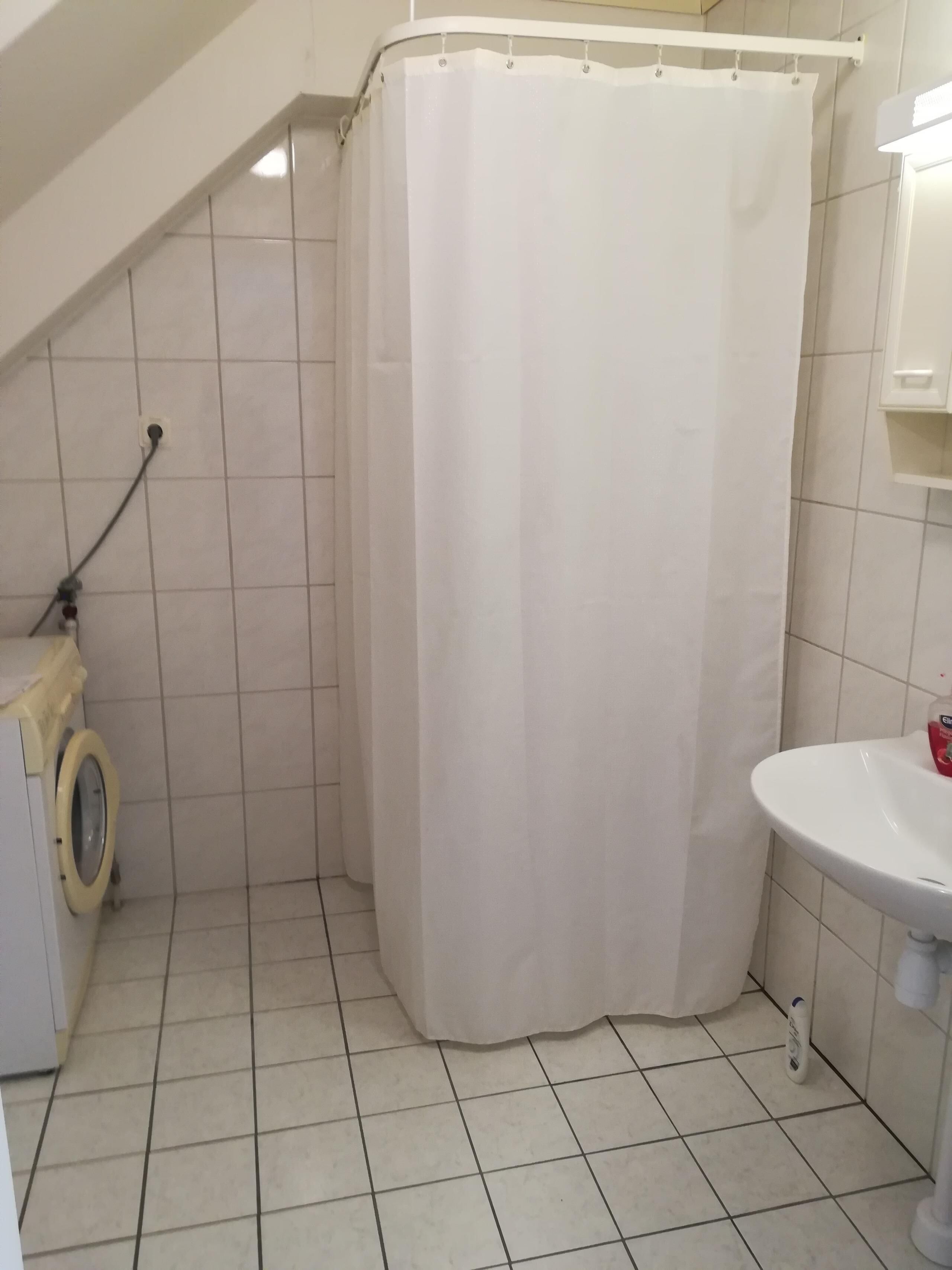 Ein kleines Badezimmer mit Fliesen, einer Duschvorhang, einer Waschmaschine und einem Waschbecken.