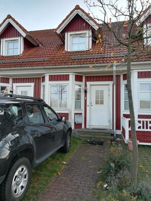 Una casa amb façana vermella i blanca, un cotxe negre estacionat al davant i un camí de maó que condueix a l'entrada.