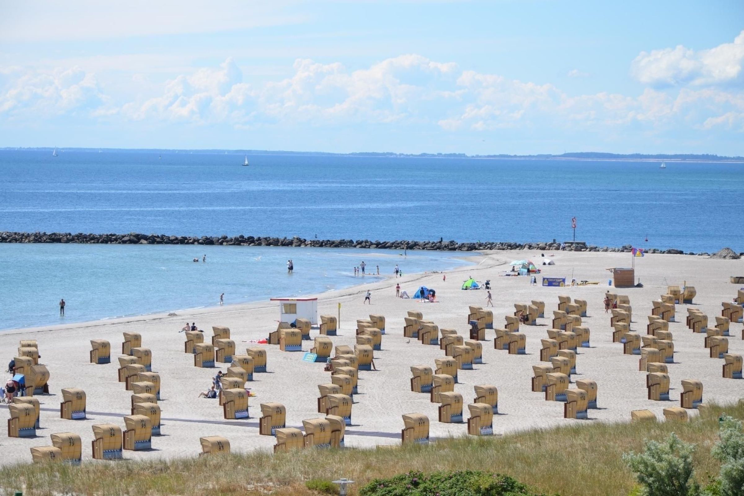 A beach with rows of wooden boxes, a rocky breakwater, and a clear blue sky.