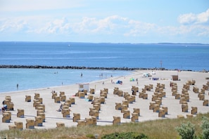 A beach with rows of wooden boxes, a rocky breakwater, and a clear blue sky. - Baltic Sea love: Your cozy vacation apartment with a fantastic sea view! (Fehmarn)