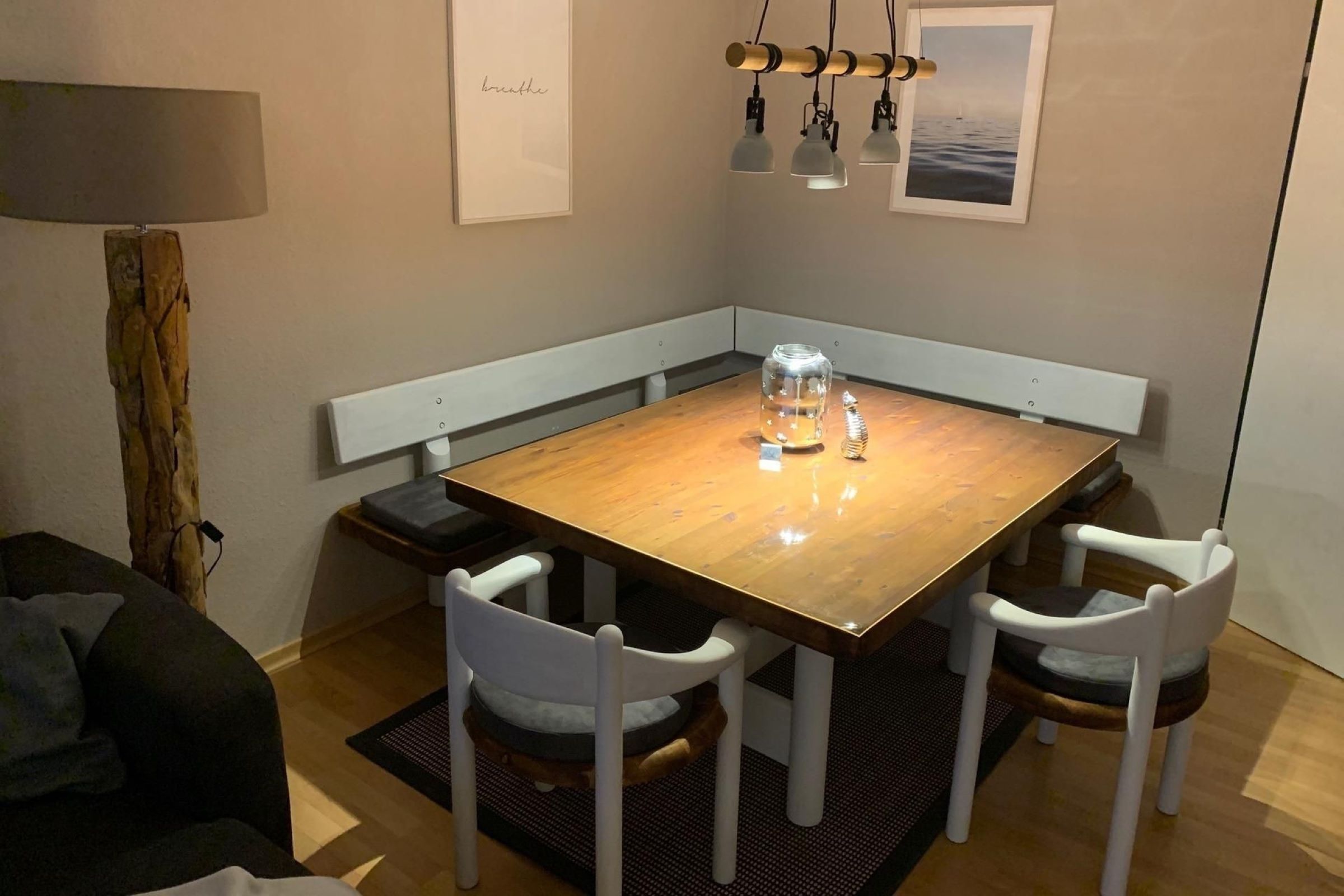A dining area with a wooden table, white chairs, a bench, and a lamp.