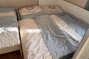 Ein Zimmer mit zwei Betten, jedes mit einem Kopfkissen, das ein nautisches Anker-Muster und den Schriftzug 'Kiistenkind' zeigt.