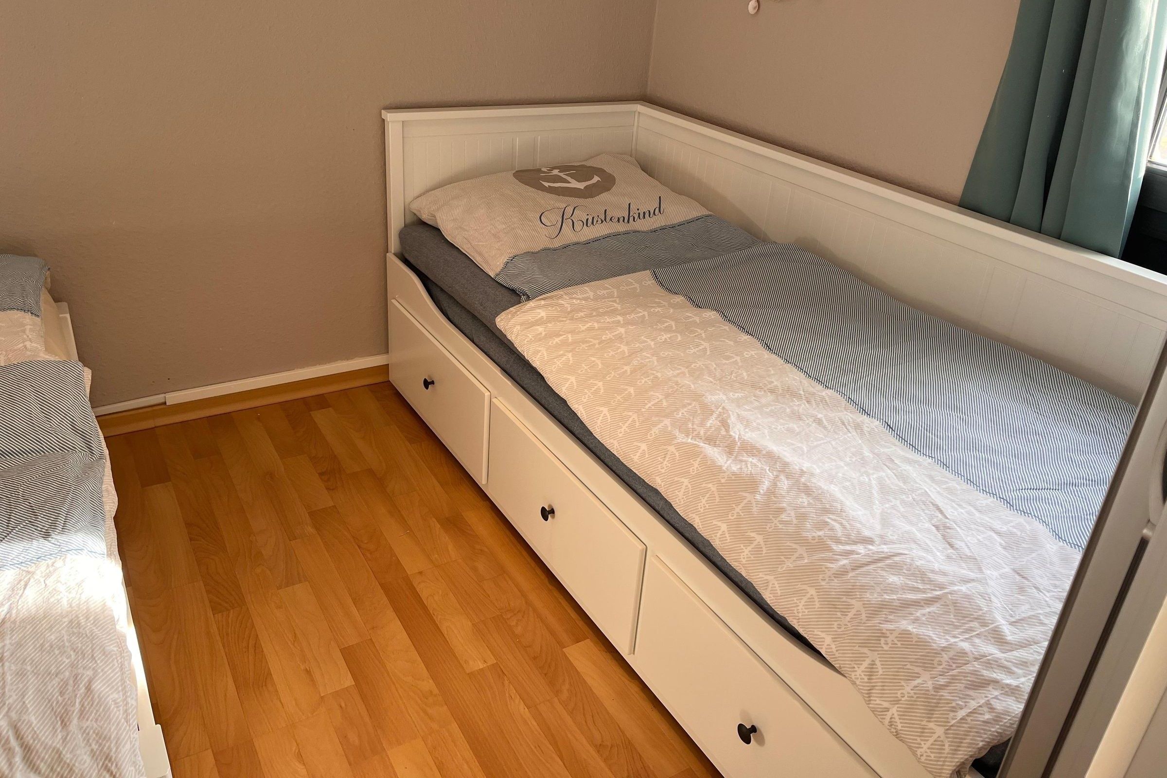 A single bed with a headboard, a bedside table, and a drawer unit.
