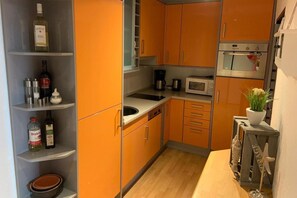 Eine kleine Küche mit orangefarbenen Schränken, einer Mikrowelle, einer Kaffeemaschine und einem Spülbecken.