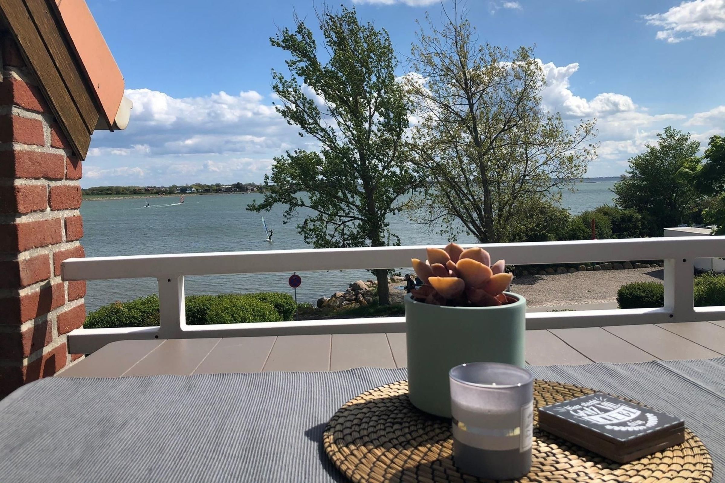 A balcony with a view of a lake, a table with a mat, a potted plant, and a candle.
